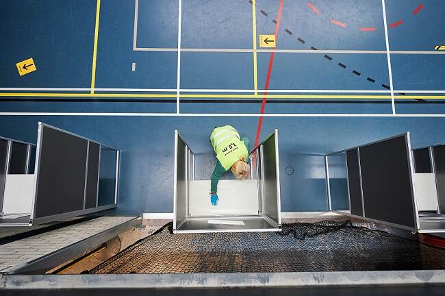 een stemhokje in een gymzaal in Boxtel wordt gereinigd door een vrouw met een geel hesje. dit is van bovenaf gefotografeerd